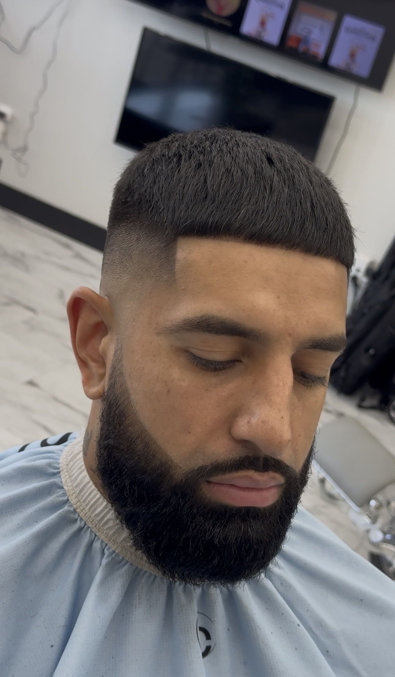A tight fade and beard, client in a light cape.